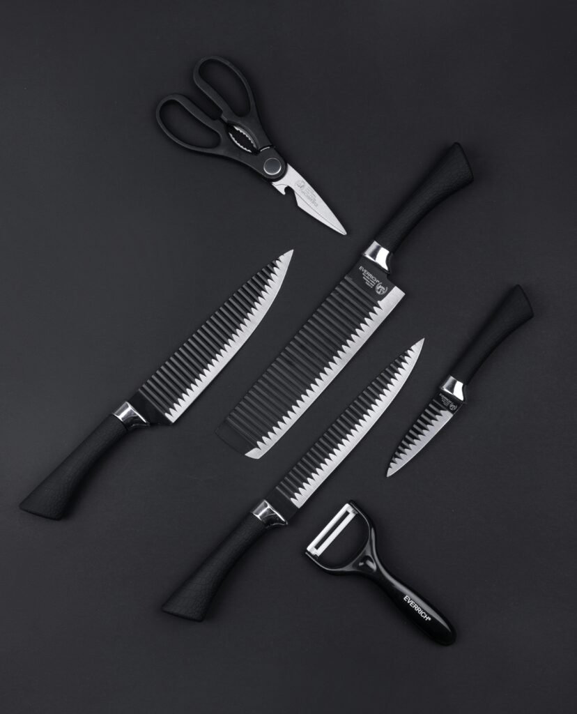 Top view of various kitchen utensils including knives scissors and vegetable peeler on black background